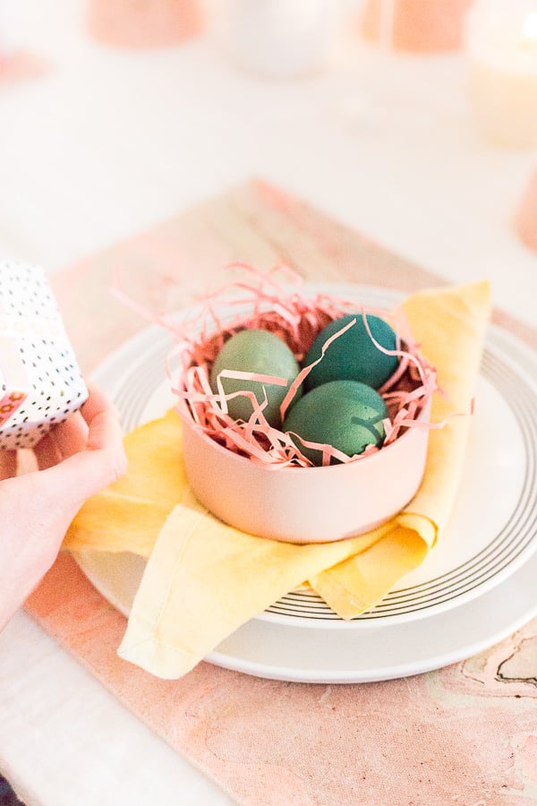 blue and green dyed easter eggs sitting in a small bowl as part of a easter table setting