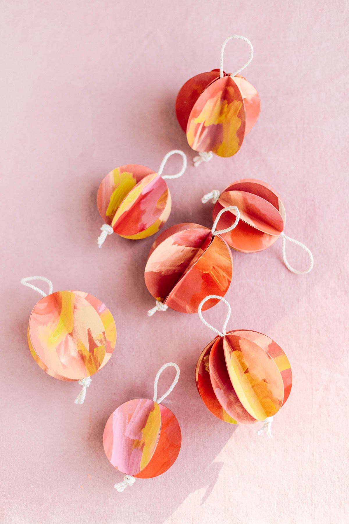 Red, pink, and yellow painted 3D ball ornaments resting on pink backdrop for the holidays