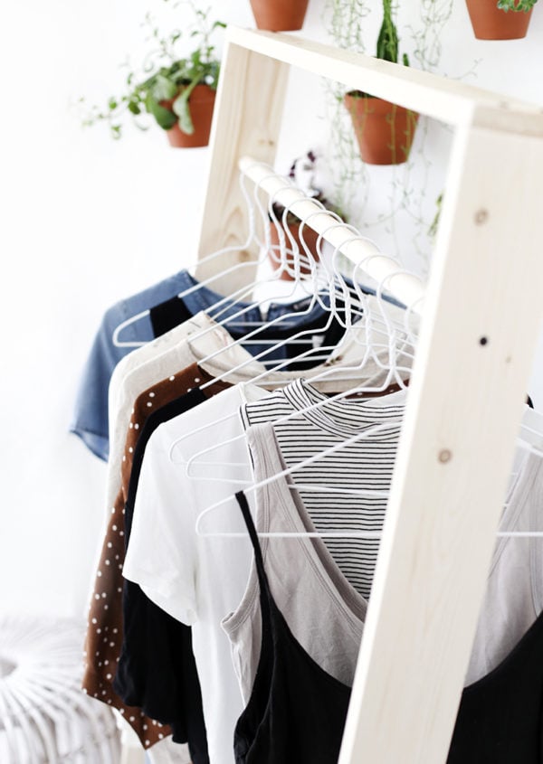 A wood clothing rack with white metal hangers hanging clothes from the clothing bar.