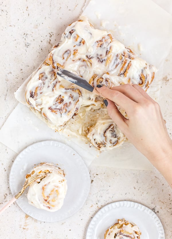 spreading icing onto pumpkin cinnamon rolls for fall