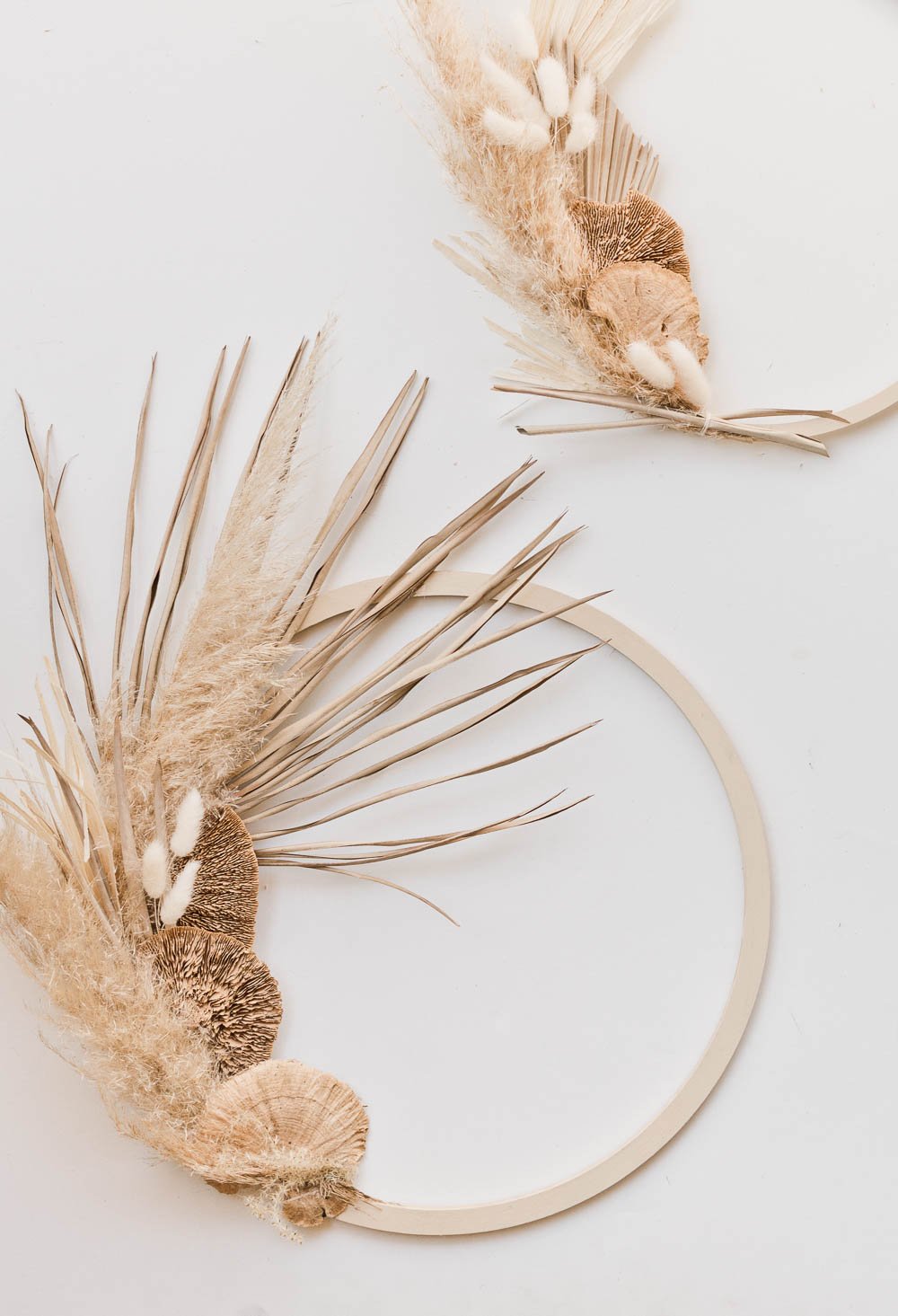 Two modern asymmetrical fall wreaths - made of pampas grass, wheat, and palm leaves.