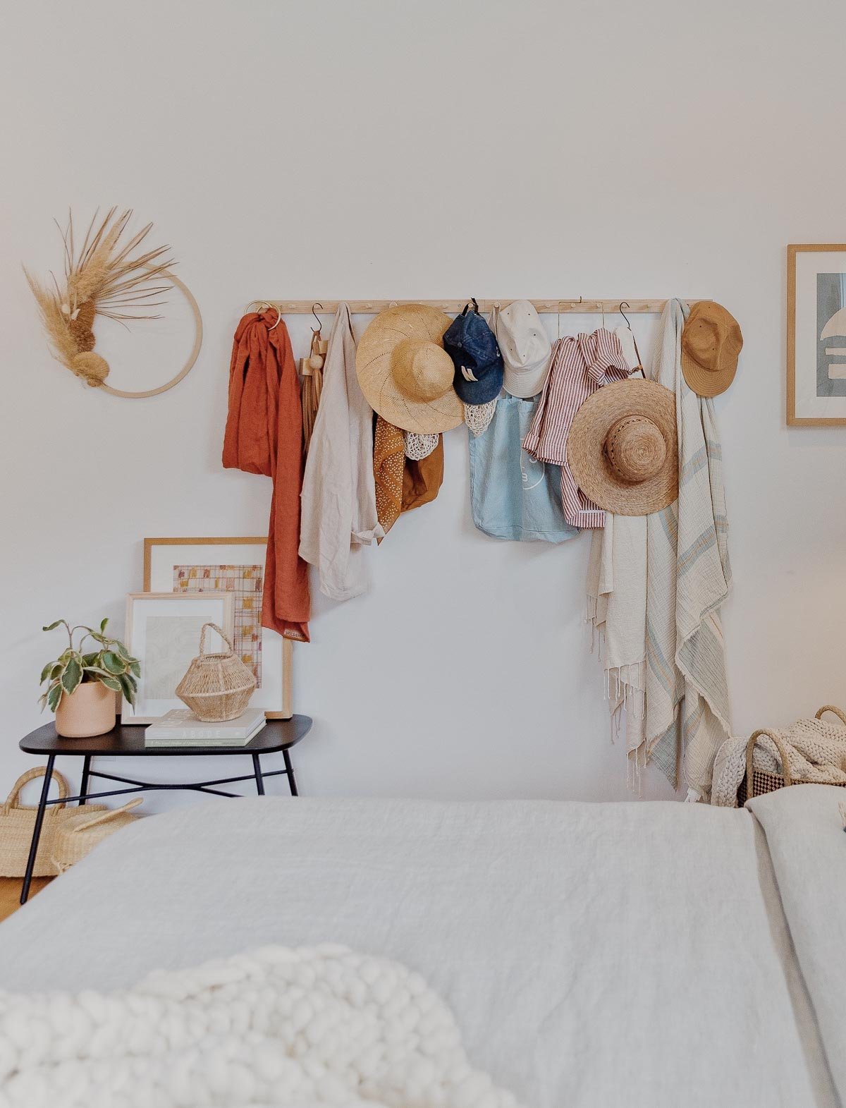 A wood peg rail hangs on a white wall with hats, scarves, and bags.