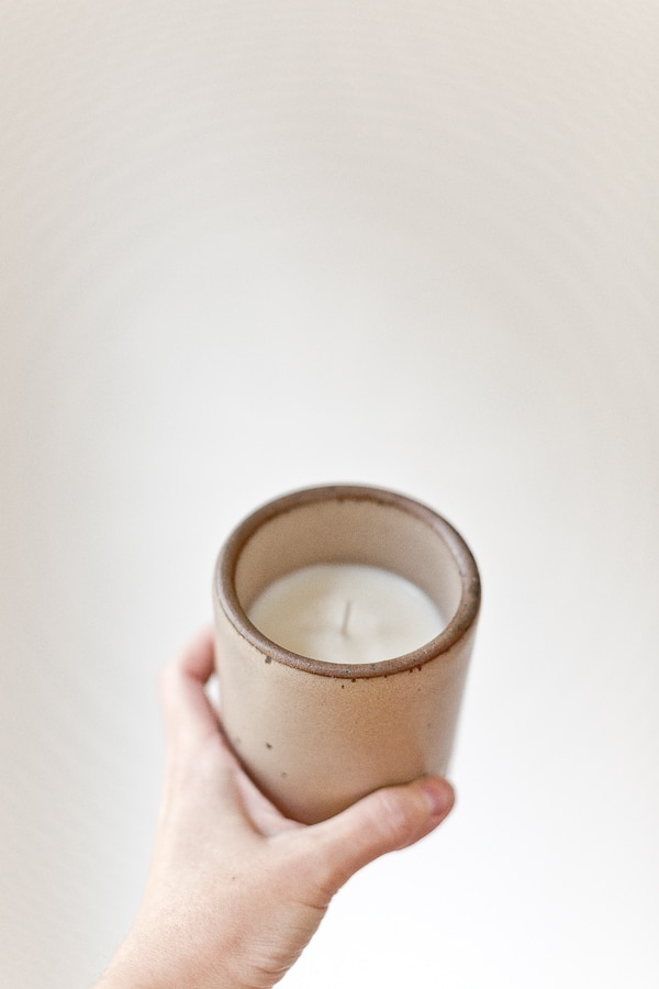 Holding homemade candle in hand against white background.