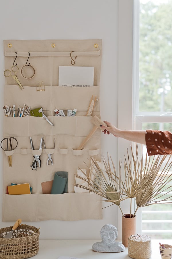 woman's hand removing art supplies from canvas wall organizer in a creative office workspace