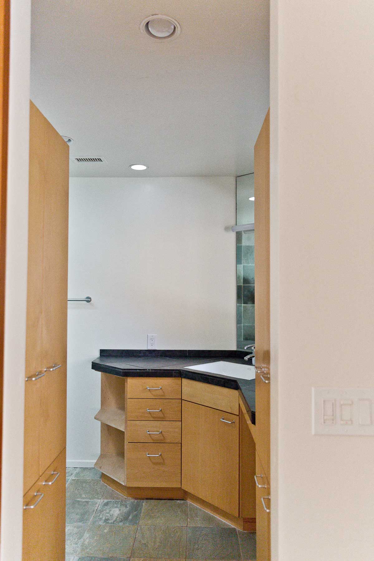 Photo of empty bathroom with wood cabinets and black natural stone counters.