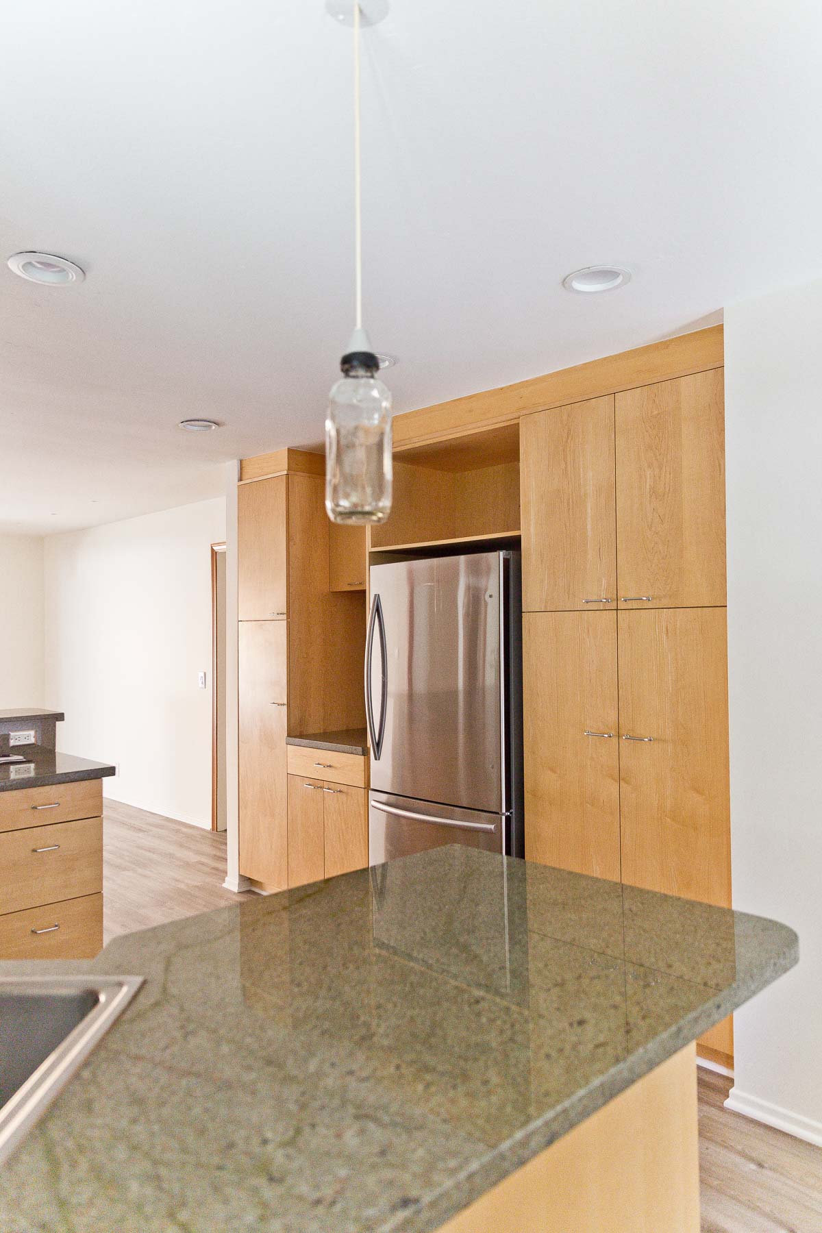 Image of empty kitchen with minimal wood cabinets and green natural stone counters.
