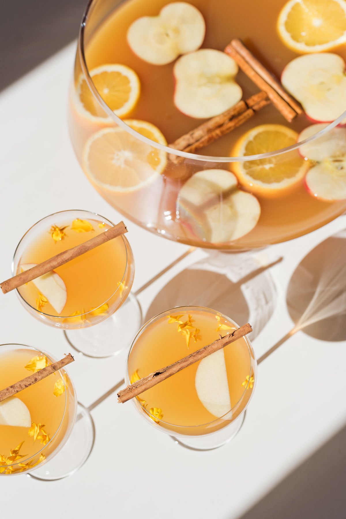 apple cider cocktails on white table, next to glass punch bowl, sunlight shining through