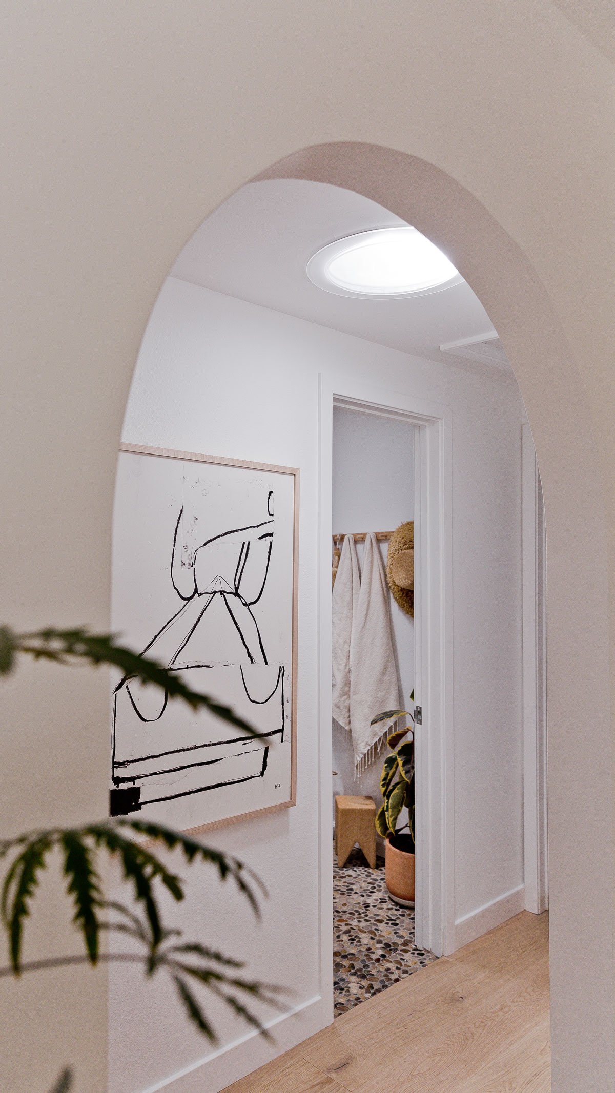 Large arch into hallway with white walls and a view of neutral earthy bathroom