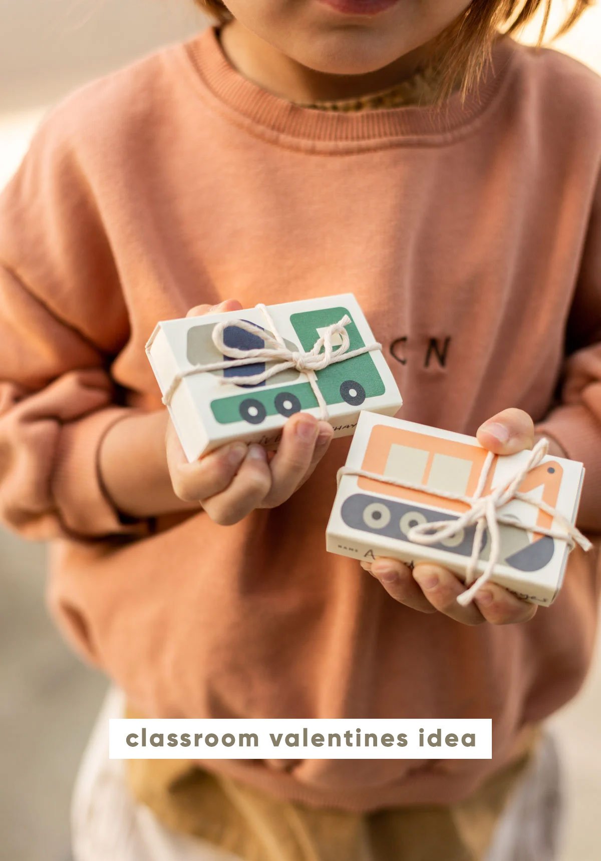 young boy holding 2 small boxes with colorful construction vehicles on each box, tied with string