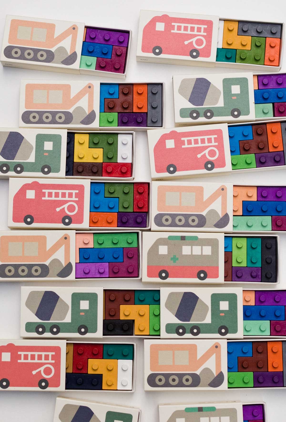 small boxes with firetrucks and construction vehicles on them, lined up, and opened to reveal colorful lego shaped crayons inside