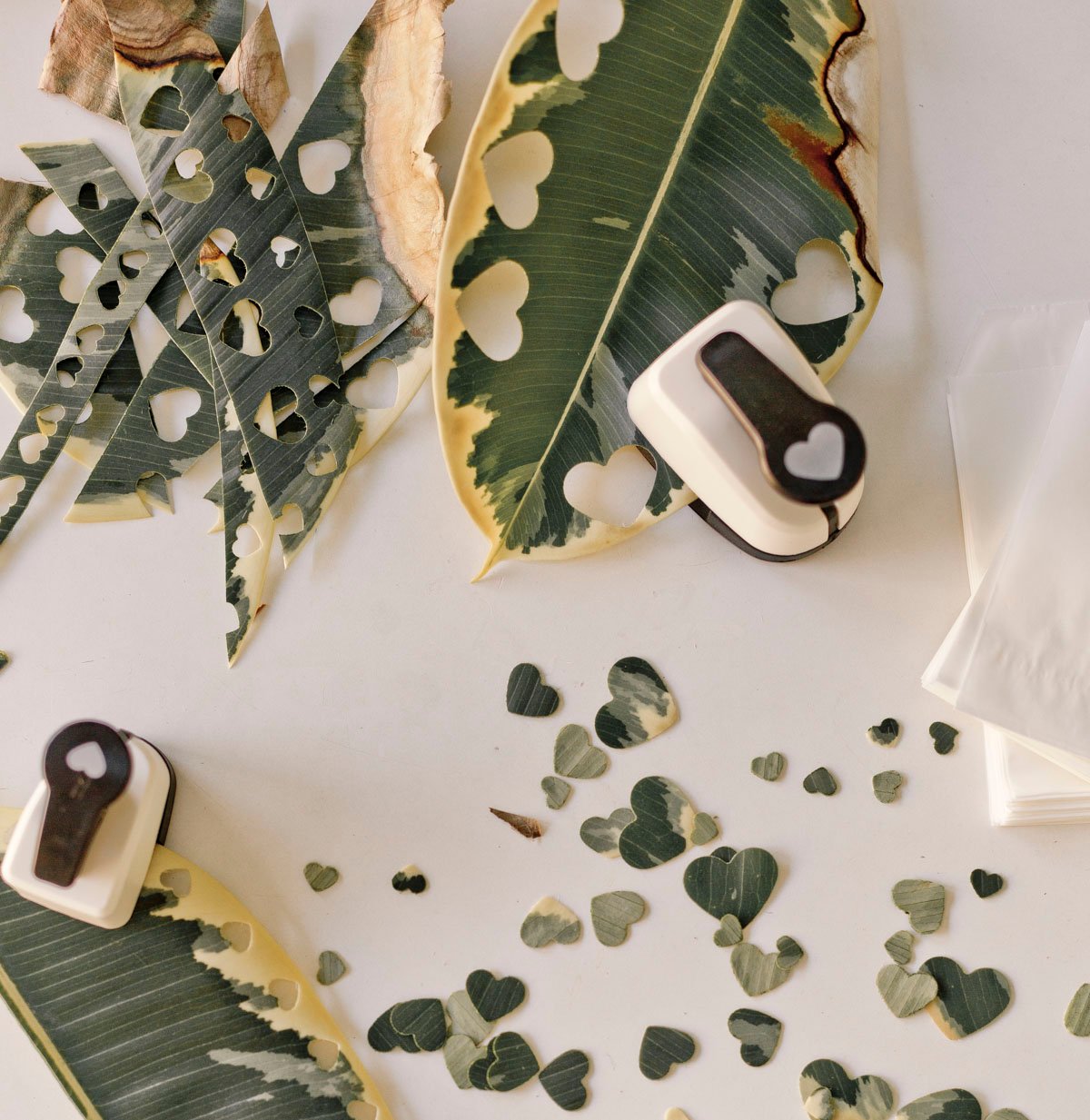 using a heart shaped hole punch to punch holes through leaves to make natural confetti for parties 