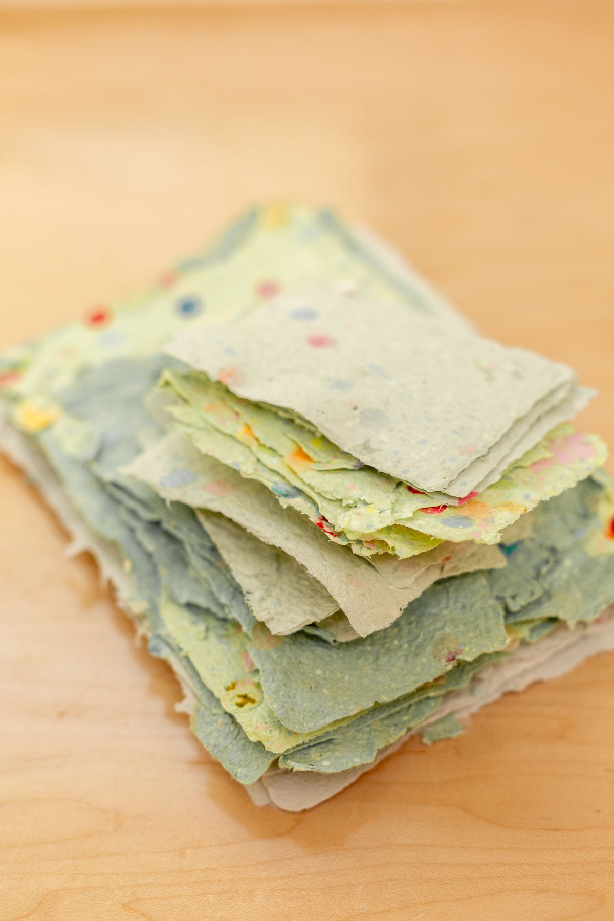 pile of homemade paper in various tones of green with rainbow colored confetti pieces inside the paper