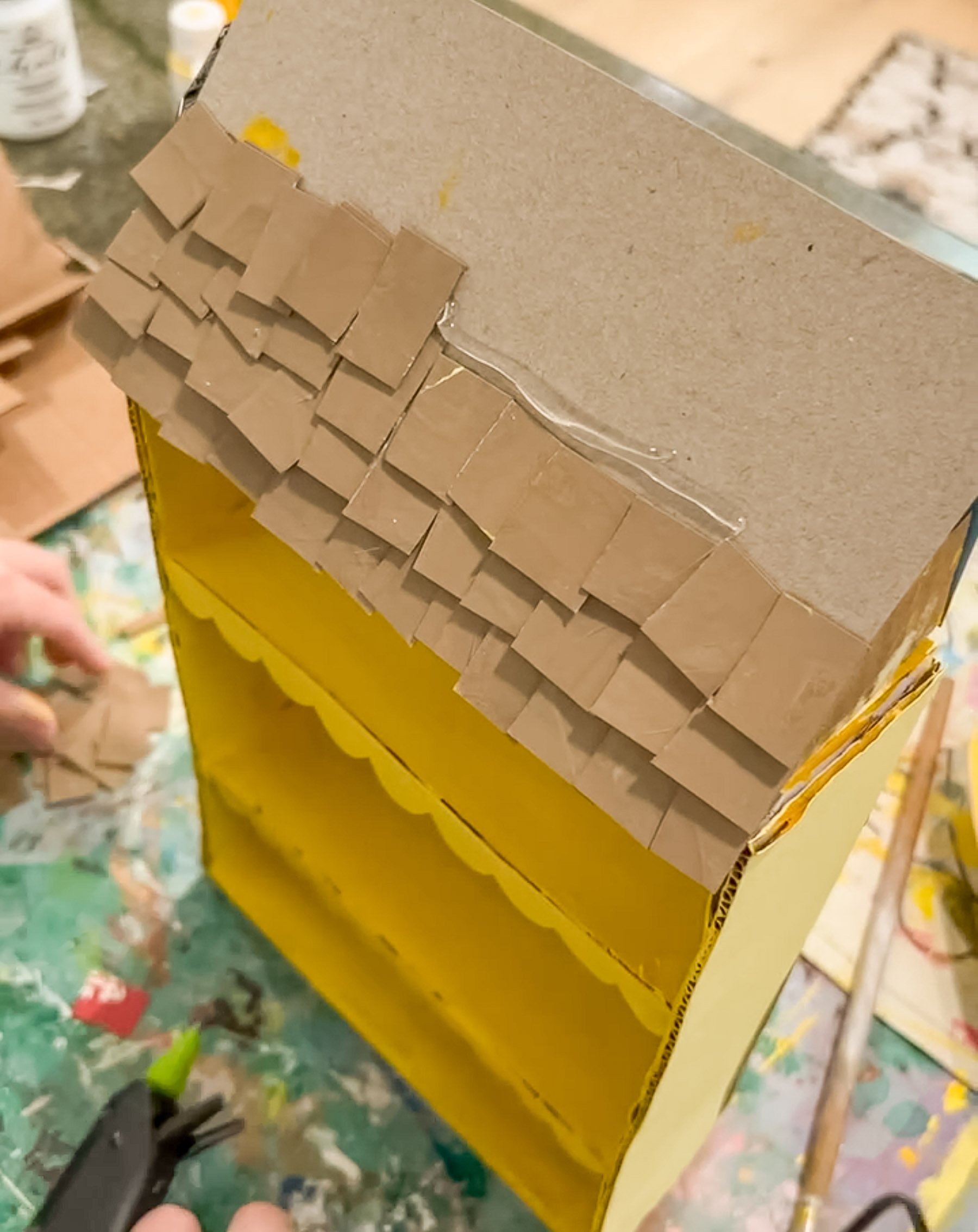 glueing cardboard shingles to a cereal box to make a roof for a dollhouse