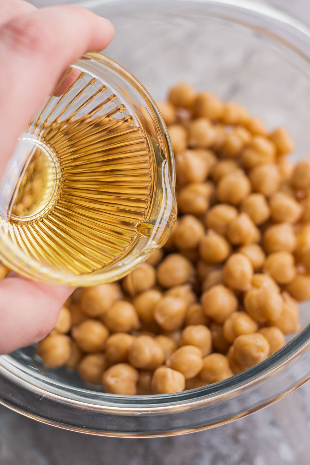 pouring small amount of olive oil over a bowl of chickpeas