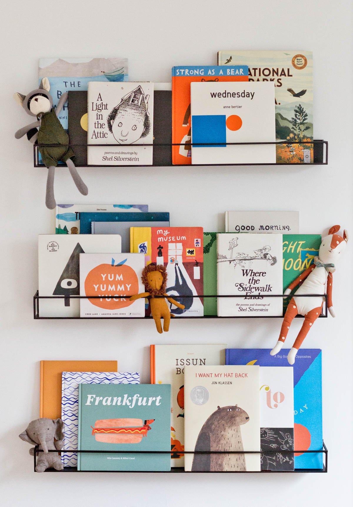 3 wall shelves in a kids room, featuring colorful children's books and some small stuffed toys