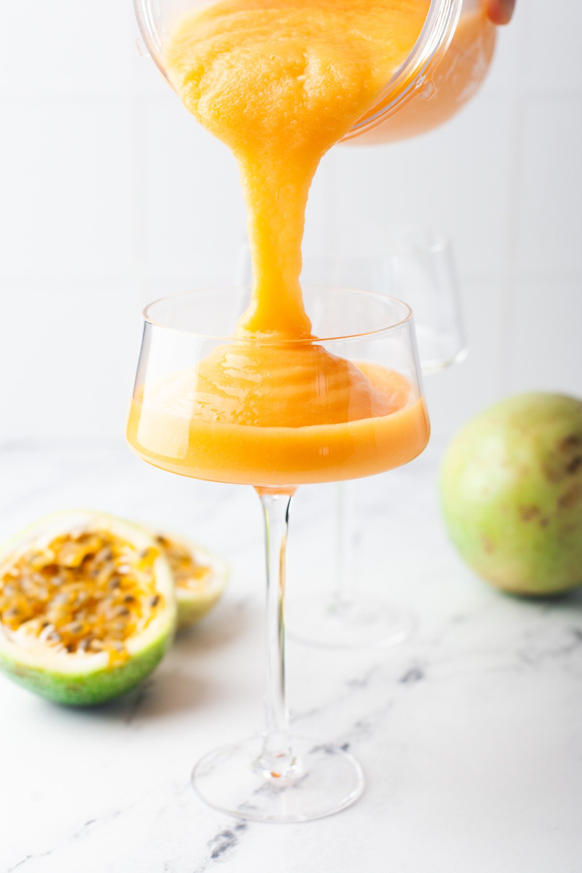 pouring a vibrant orange and yellow frozen aperol spritz cocktail into a clear glass with a tall stem
