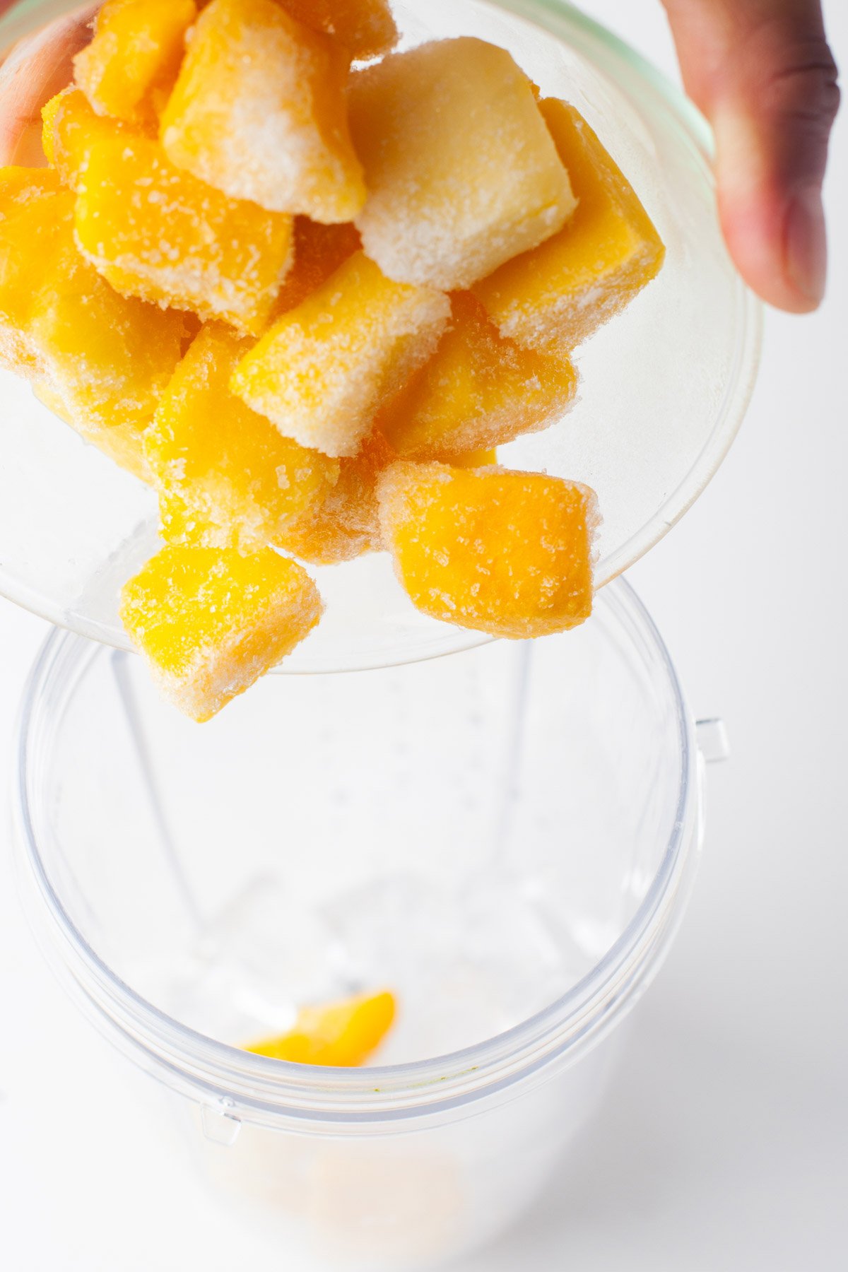 pouring frozen mango into a blender