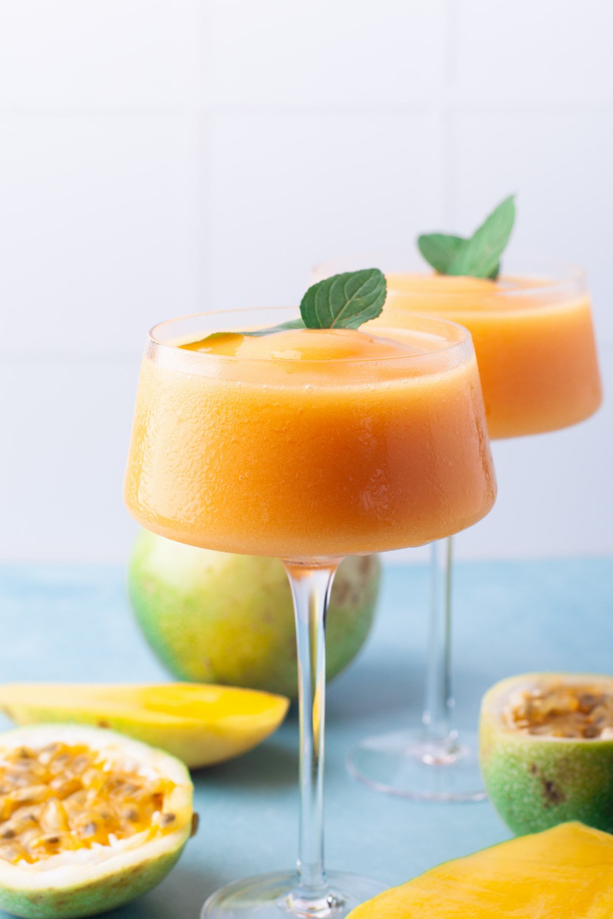 two orange frozen cocktails in tall stemware on counter with fruit