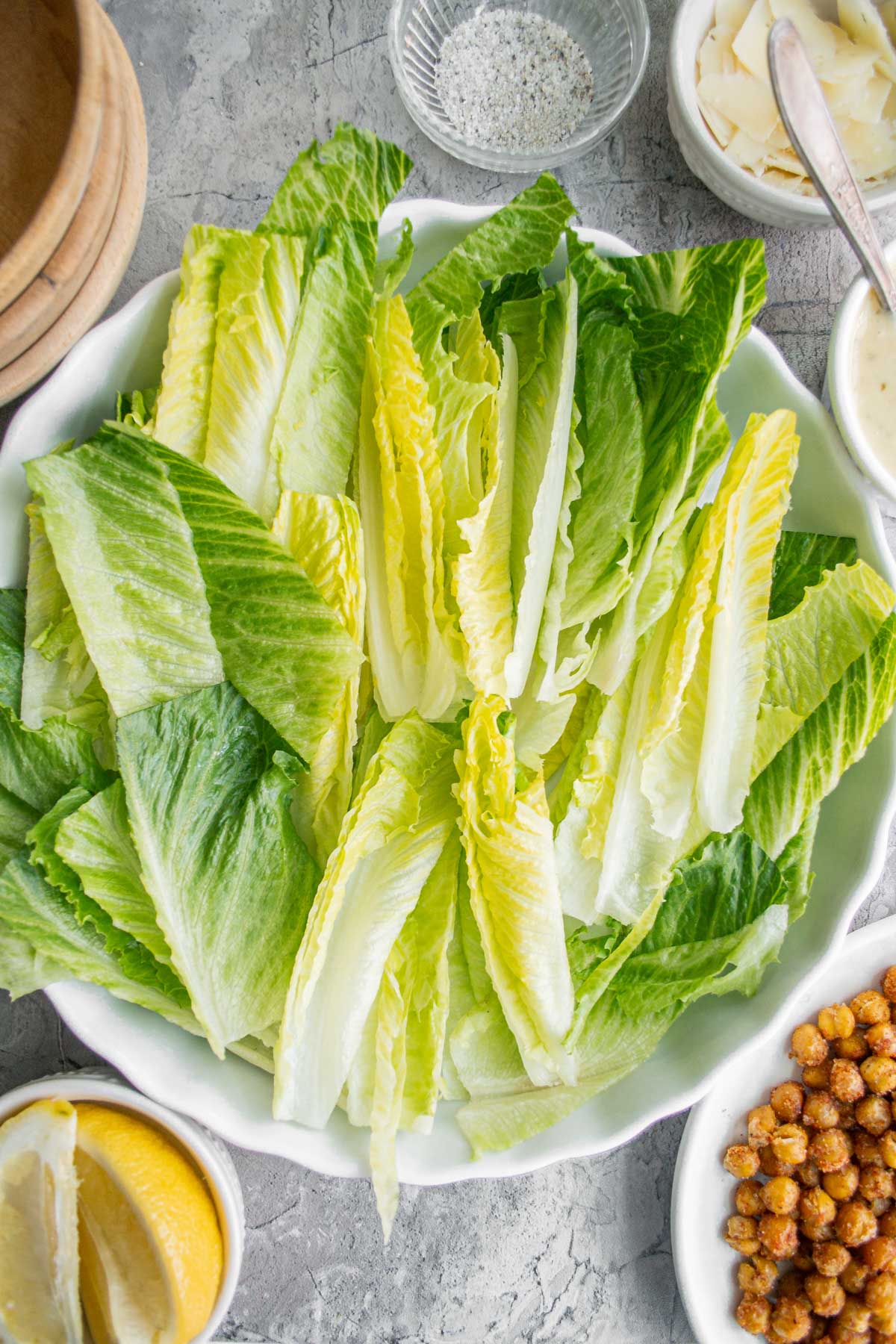 bowl of romaine and roasted chickpeas and lemons on a counter with plates and other ingredients 