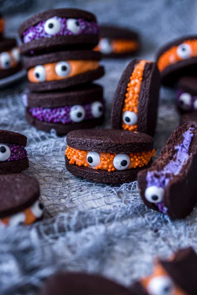 halloween cookie sandwiches with chocolate cookies and sprinkled icing on the inside with candy eyes in the middle