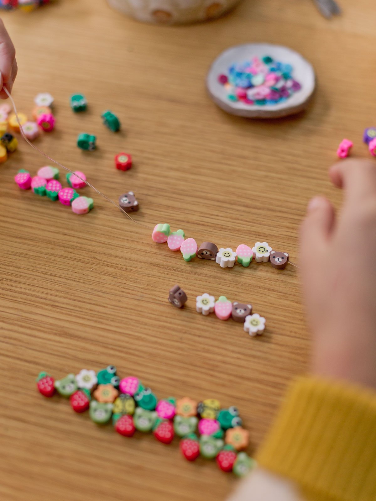 child putting together a colorful beaded bracelet by stringing clay beads onto a clear string