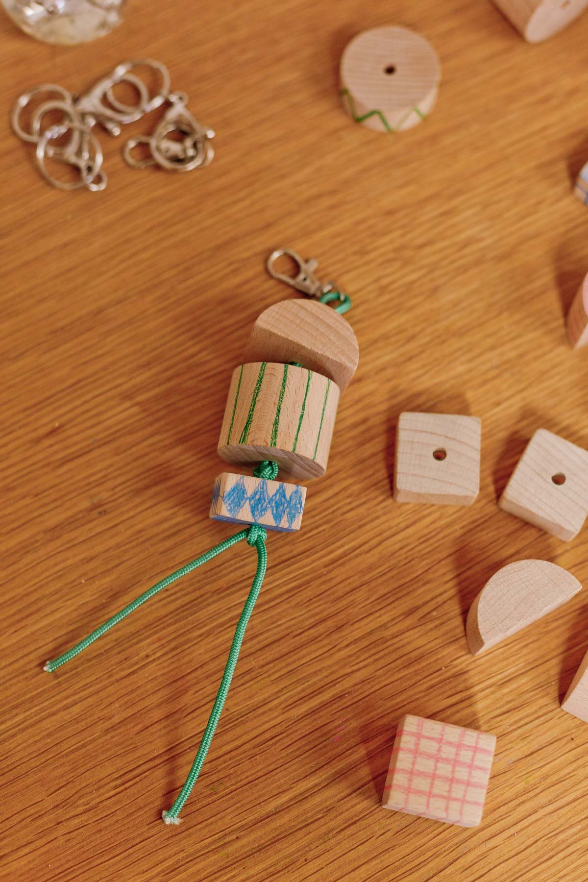 chunky wood keychain with green cording and simple patterns drawn onto blocks