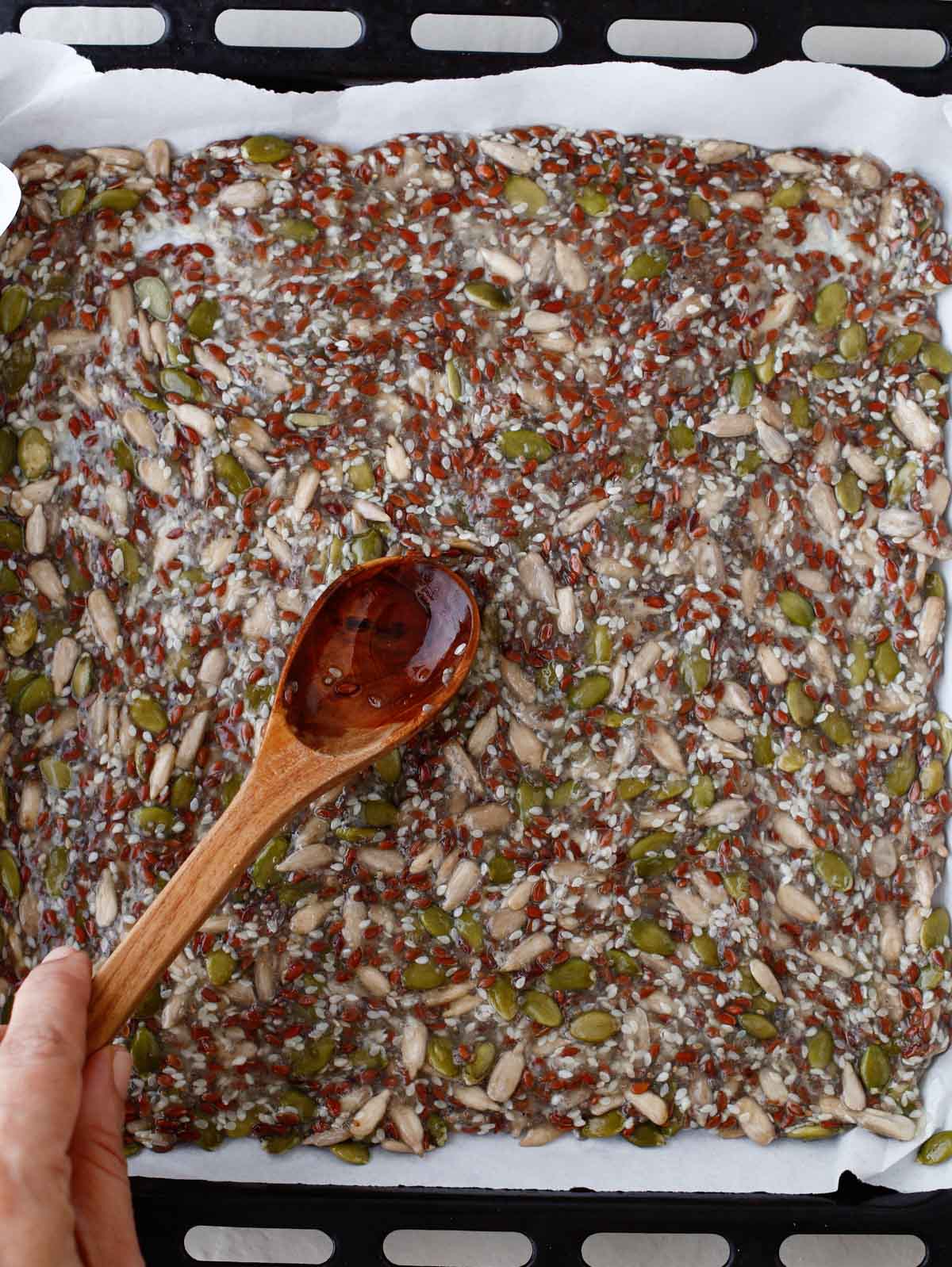 spreading seed cracker mixture out onto a sheet pan with wooden spoon
