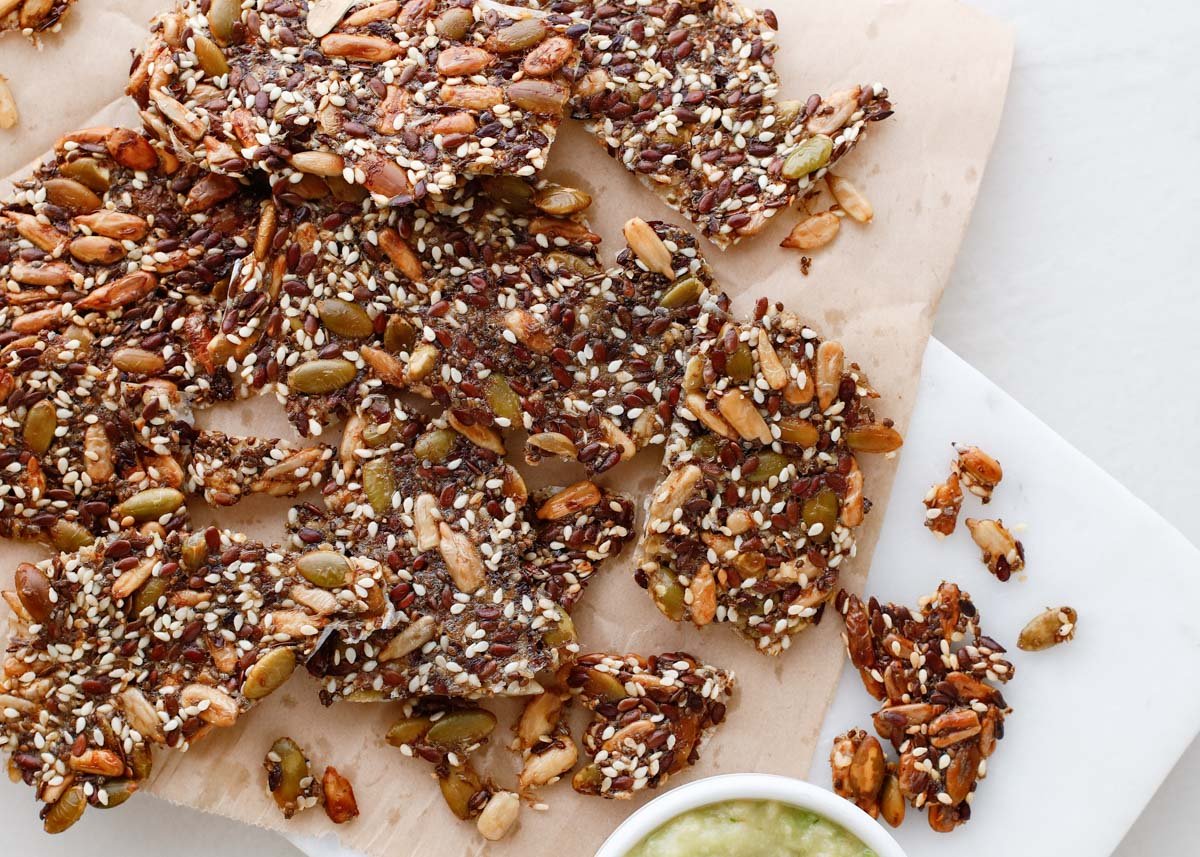 brown seed crackers in small pieces with green spread in small bowl nearby
