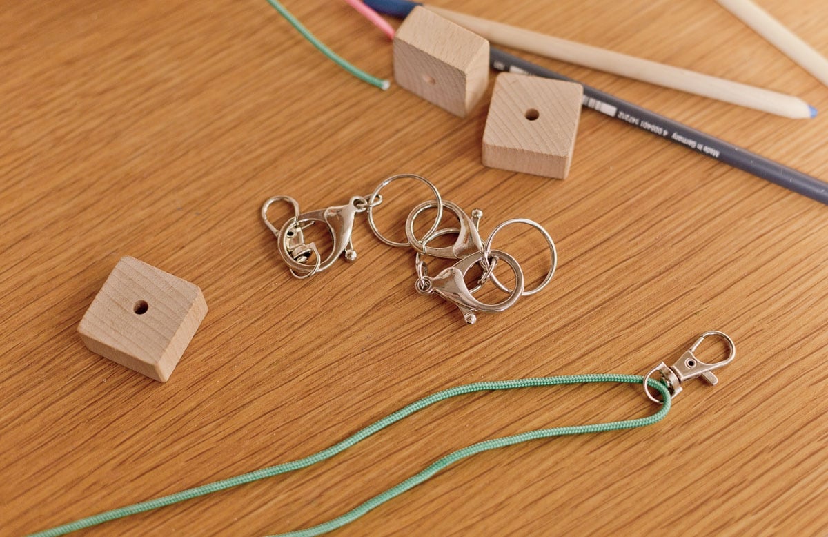 green cording and keychain lobster clasp being threaded onto cord with wood blocks nearby