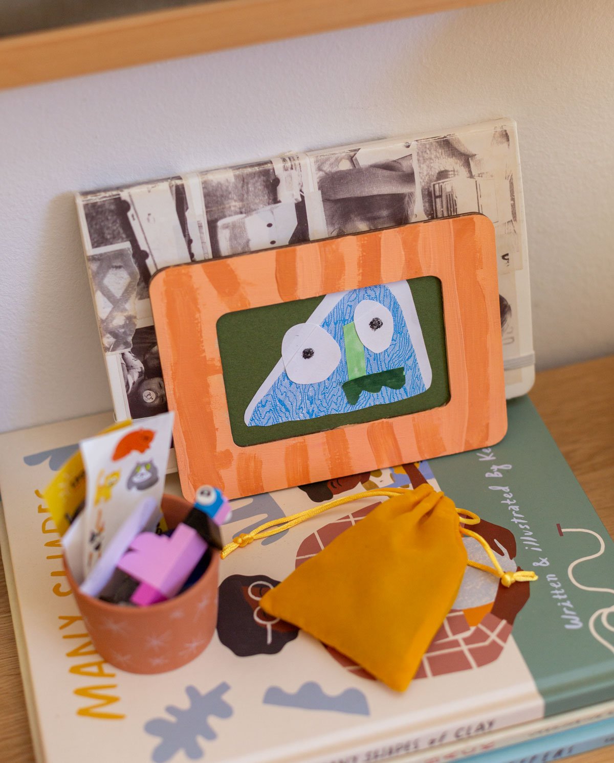 framed kids monster art made from junk mail, sitting on a stack of books in cool kids bedroom