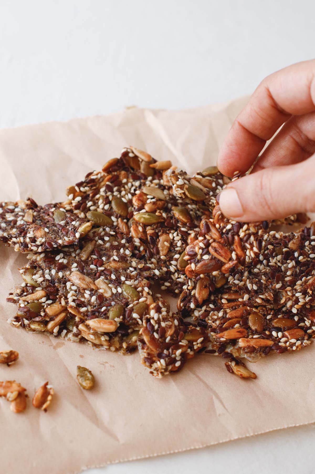 person grabbing small homemade seed cracker from pile on a cracker board