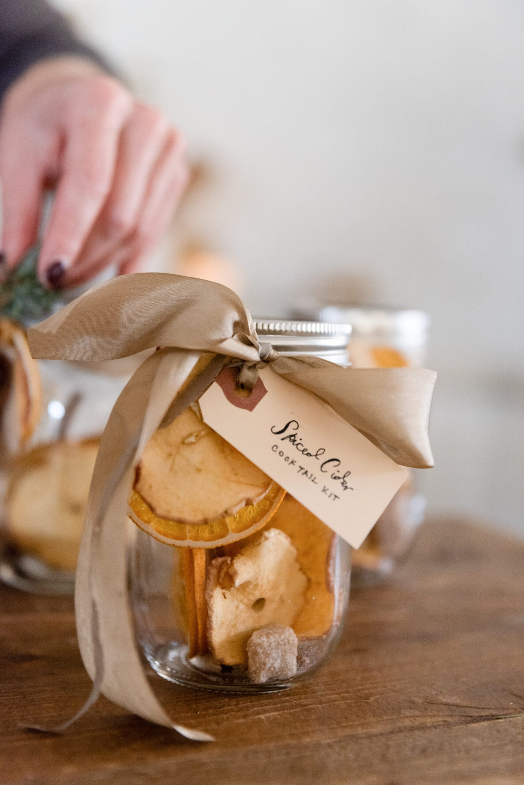 spiced cider cocktail jar gift, with a woman adding a silk ribbon