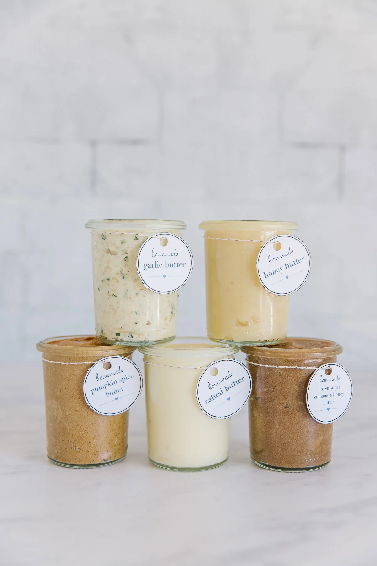 five glass jars stacked on top of each other, each with a different flavor of butter in each one
