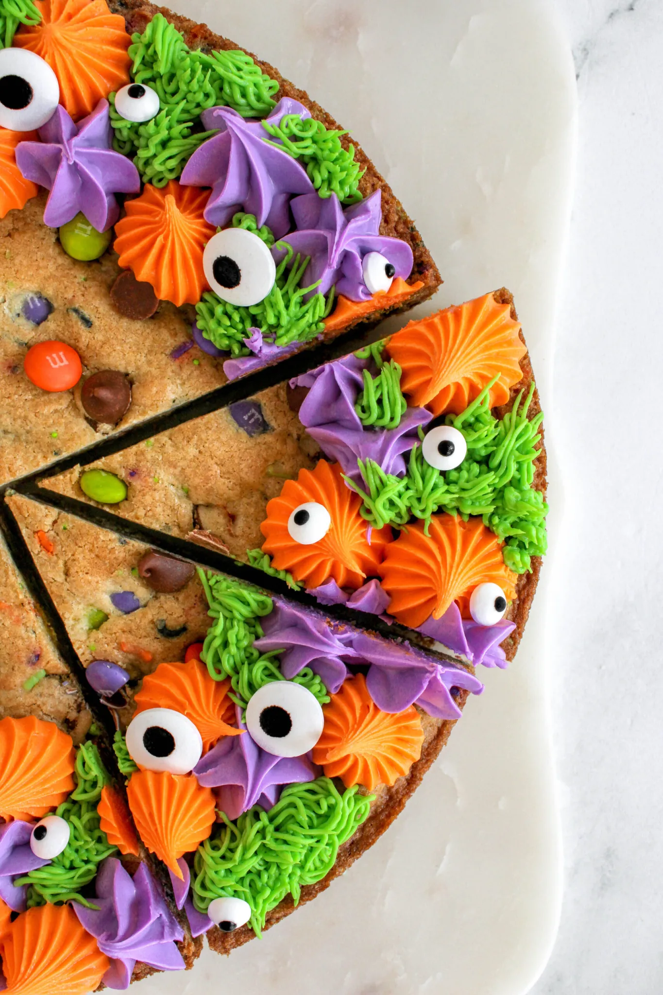 closeup of large cookie cake with colorful frosting details and halloween inspired googly eyes candy