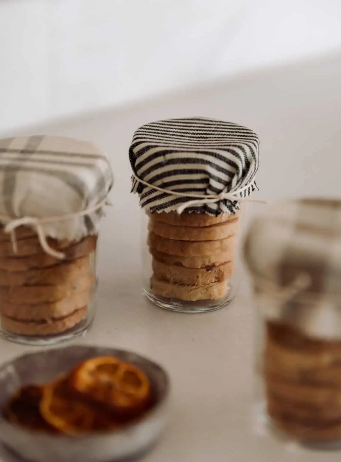 small stacked cookies in glass jars with fabric over the top and string