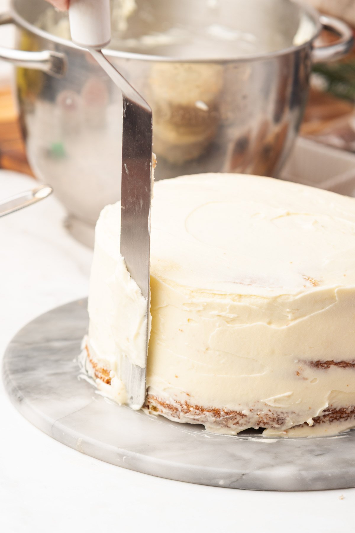 crumb coating christmas cake with cream cheese frosting and a spatula