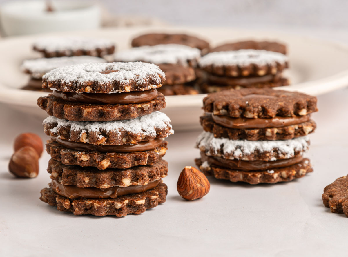 stacked chocolate linzer cookies with hazelnuts and powdered sugar