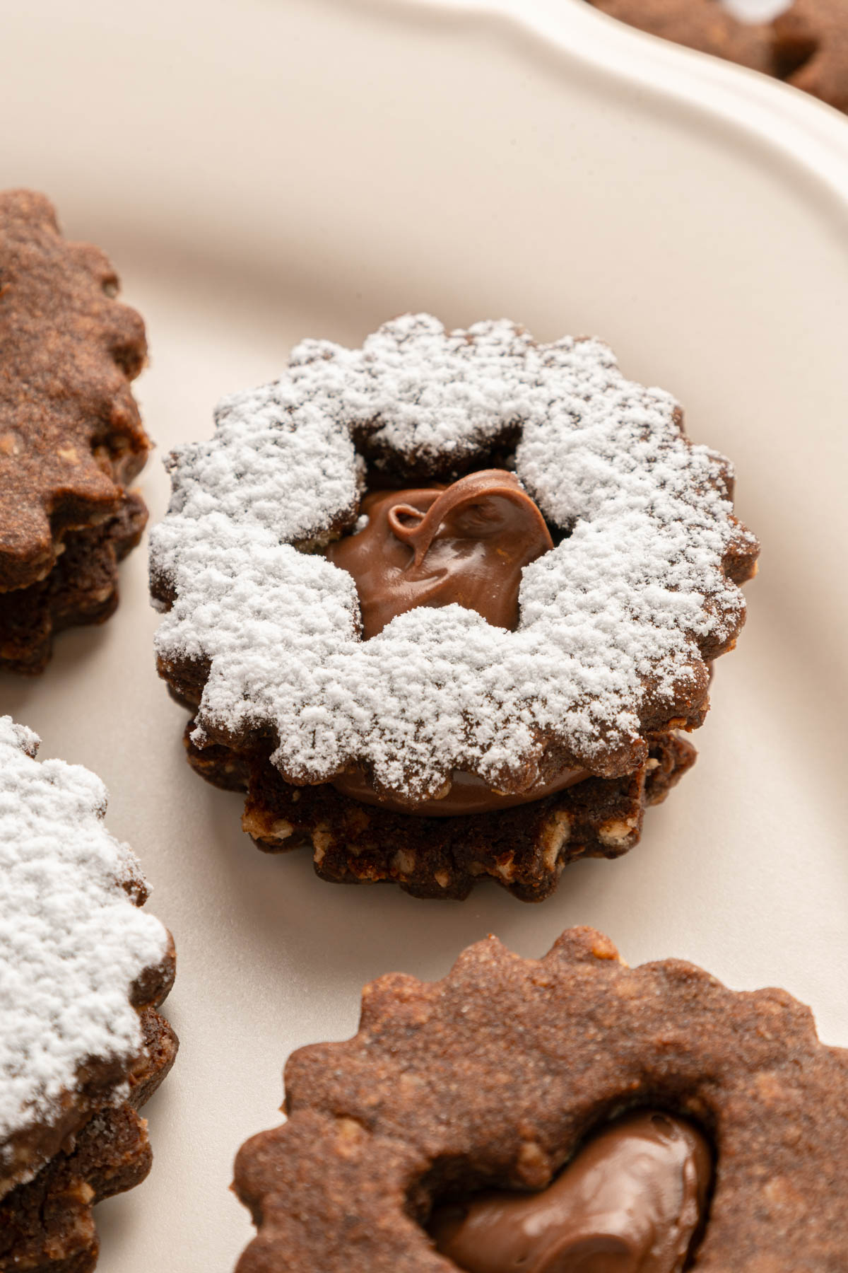 closeup of chocolate linzer cookies on a beige plate, with powdered sugar on top