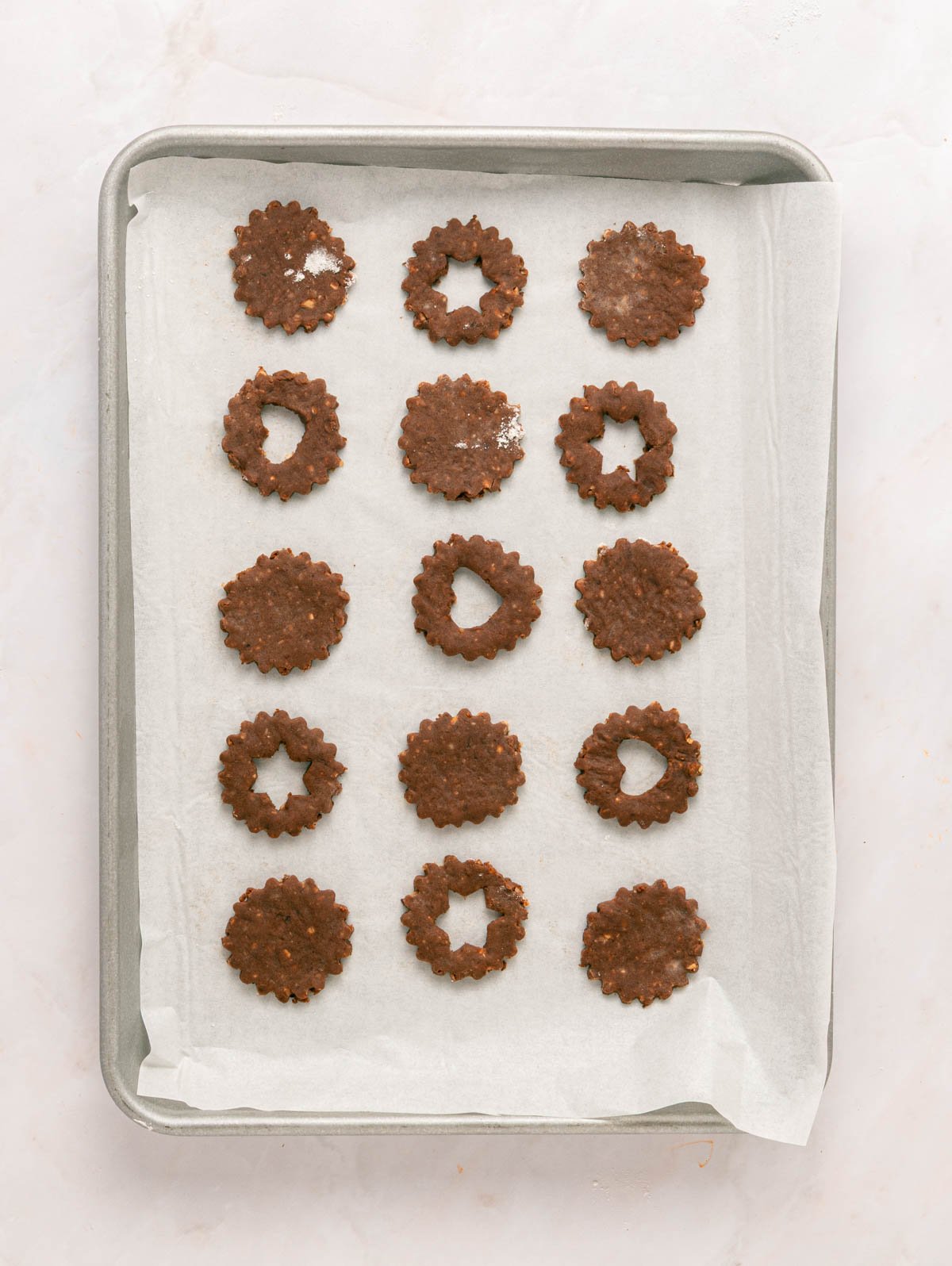 chocolate linzer cookies on a baking sheet, lined up and ready to bake