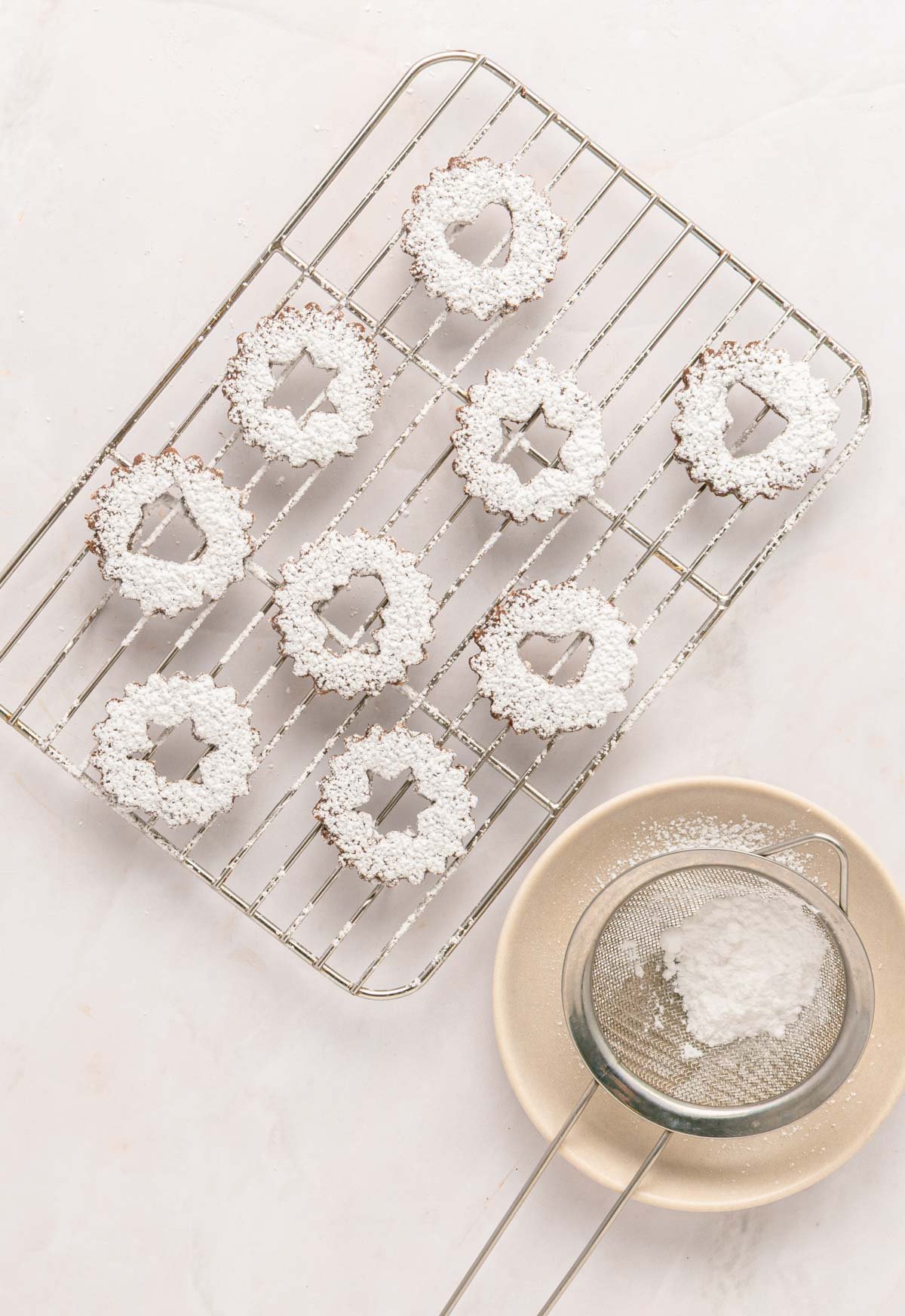 linzer cookies being topped with powdered sugar on a cooling rack