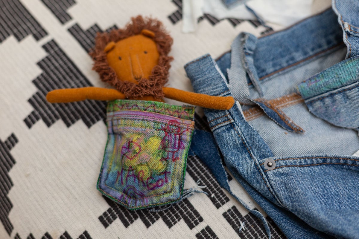 small denim pouch with kids doodles and a small stuffed lion inside