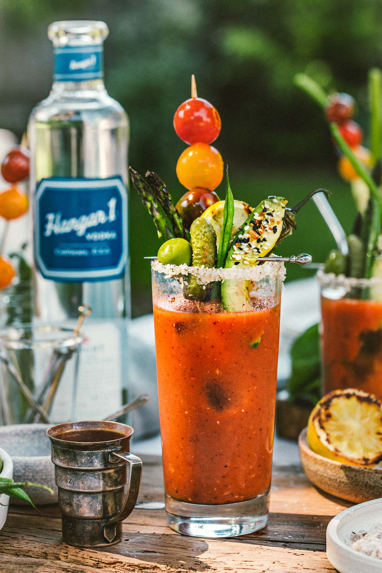 bloody mary cocktail in tall glass with fresh veggie garnishes and other items on a dinner table outdoors