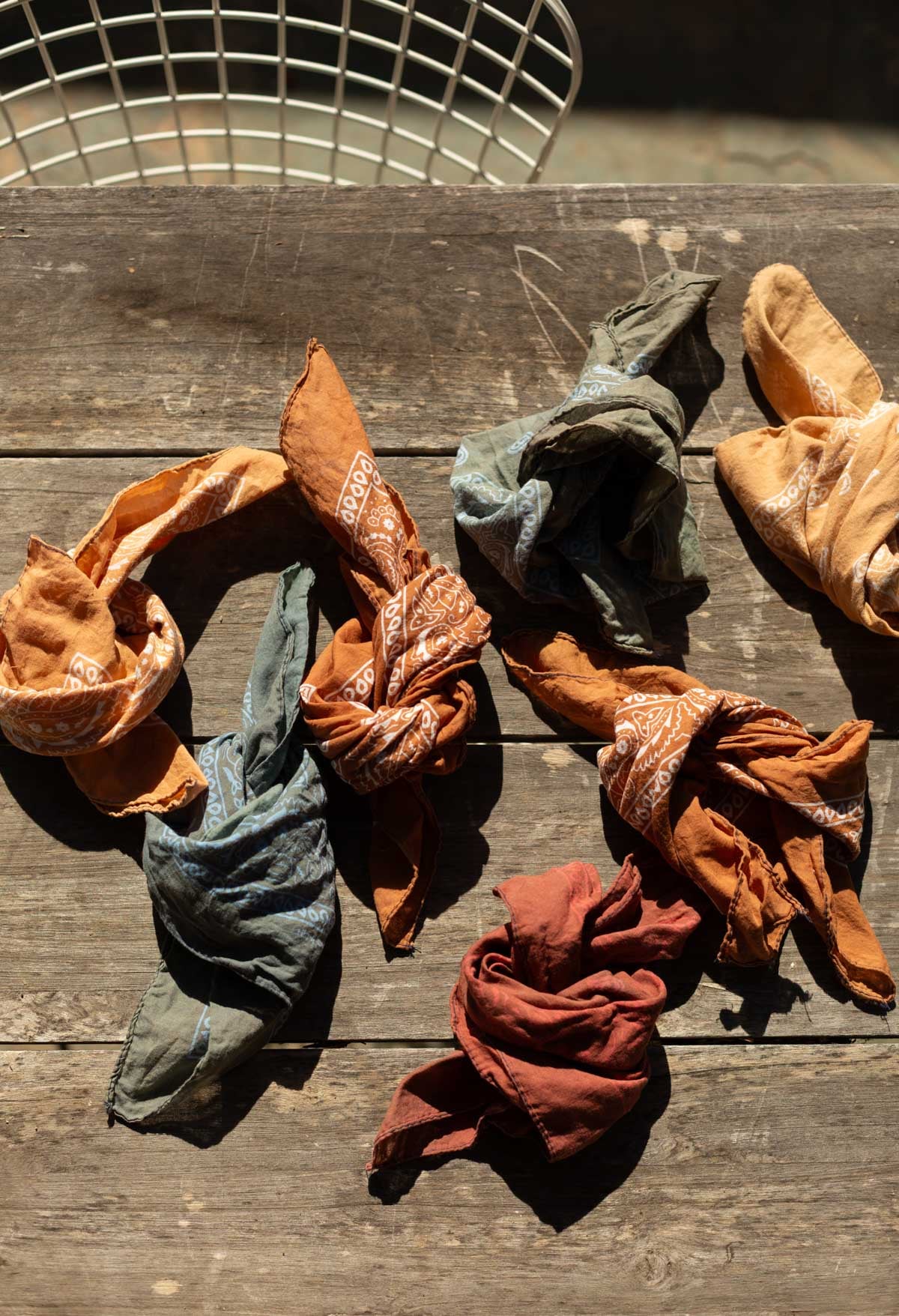 earth tone bandanas tied up in knots on an old table outdoors