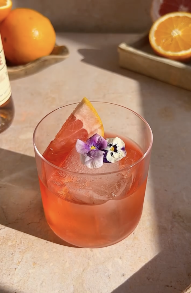 pink drink in short modern glass with edible flowers and grapefruit garnish