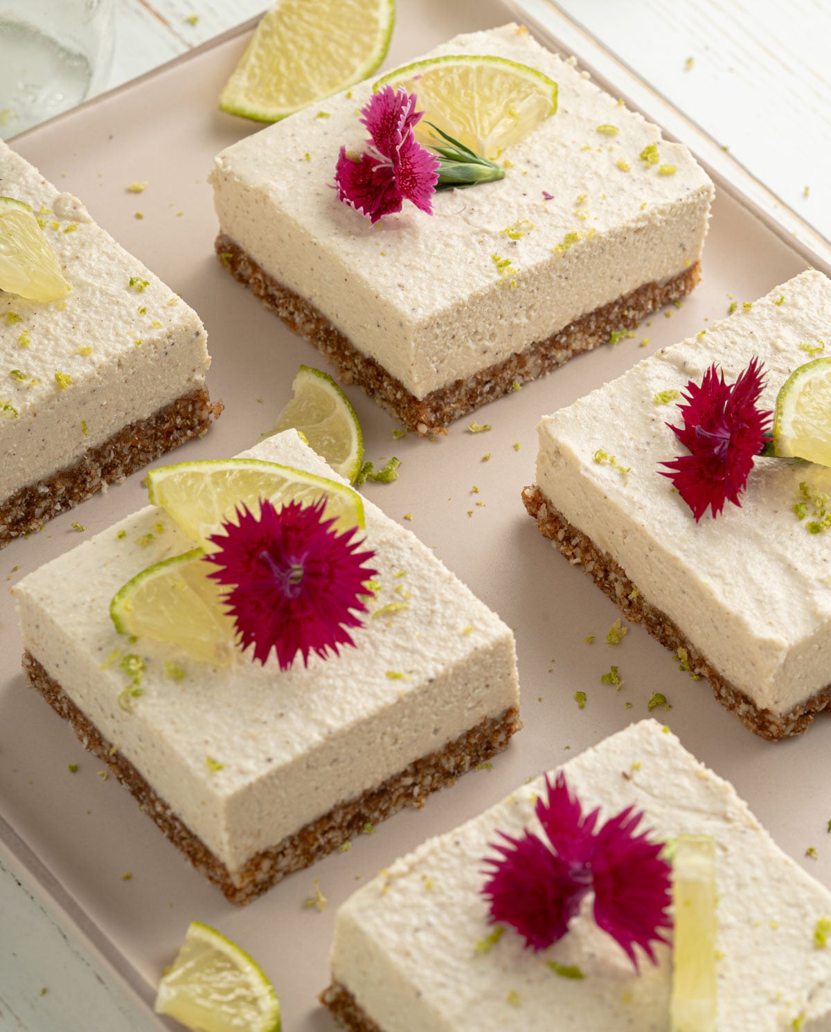 key lime bars cut into squares on a tray with lime slices and edible flowers